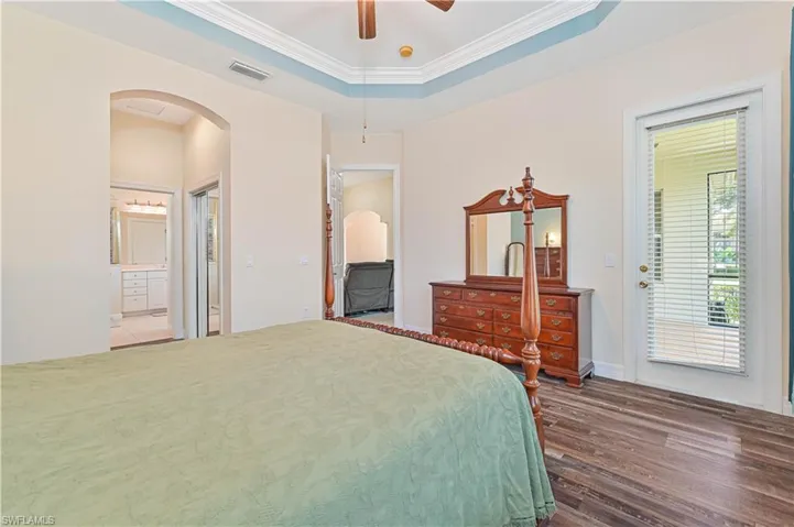 Bedroom featuring a tray ceiling, arched walkways, crown molding, access to exterior, and dark wood-style flooring