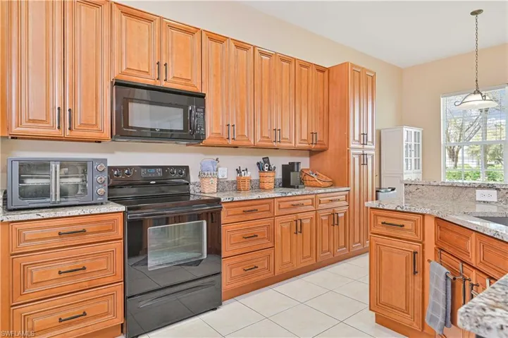 Kitchen featuring black appliances, light stone counters, pendant lighting, and wood finish cabinetry