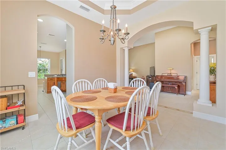 Dining area with a raised ceiling, ornate columns, arched walkways, light tile patterned floors, and suspended lighting