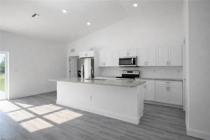 Bright kitchen space featuring white shaker cabinetry, stainless steel appliances, a central island with a granite-style countertop, and wood-finish flooring