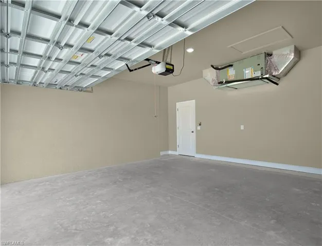 Spacious garage featuring a concrete floor, light-toned walls, and a white interior door