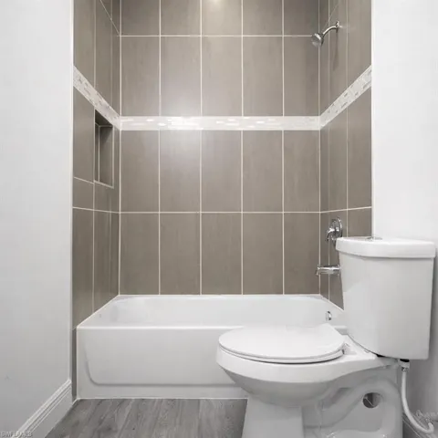 Bathroom featuring a white bathtub, gray rectangular wall tiles with a decorative mosaic accent band, a built-in shower niche, and a chrome shower fixture