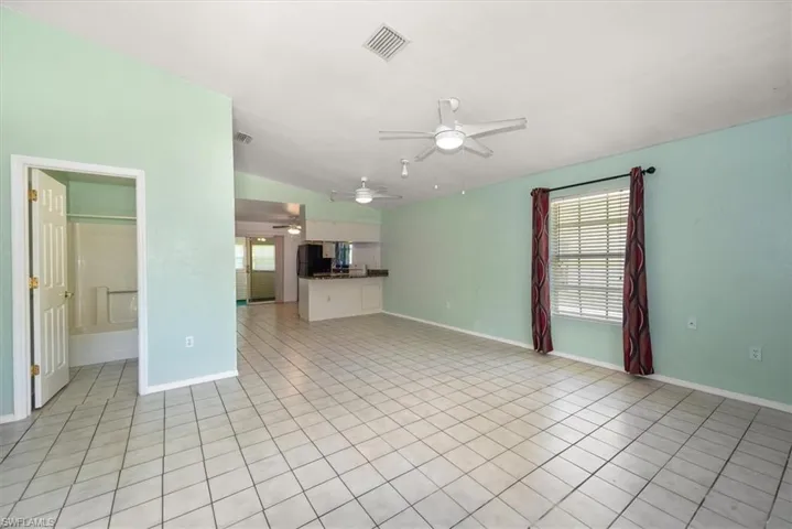 Unfurnished living room with a ceiling fan, vaulted ceiling, and light tile patterned floors
