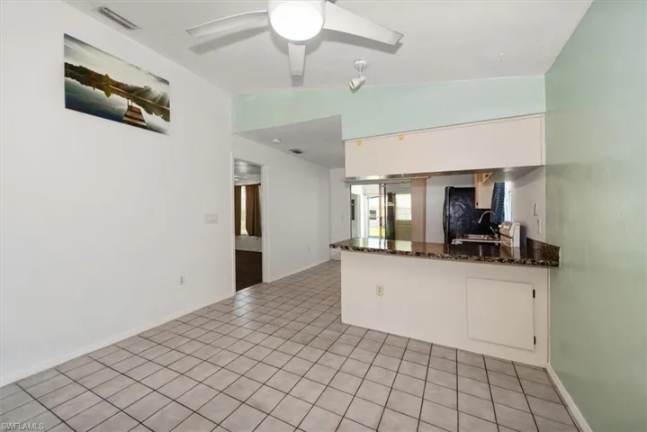 Kitchen with lofted ceiling, light tile patterned floors, dark stone counters, a peninsula, and a ceiling fan