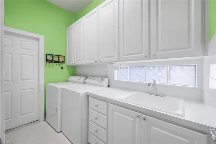 Laundry area with cabinets, independent washer and dryer, sink, and light tile patterned floors