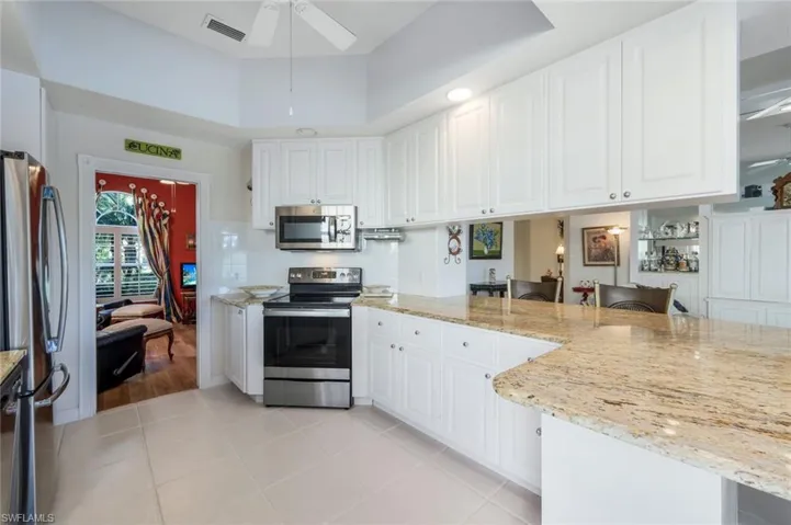 Kitchen with white cabinets, ceiling fan, light stone counters, kitchen peninsula, and stainless steel appliances