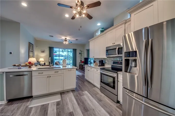 Kitchen featuring sink, decorative backsplash, ceiling fan, light hardwood / wood-style floors, and stainless steel appliances