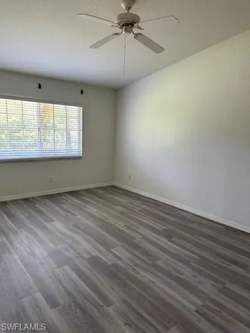 Spacious room featuring wood-finish plank flooring, a white ceiling fan with light fixture, and a window with blinds