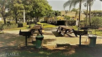 Outdoor grilling area featuring a paver patio, two picnic tables, and mature trees