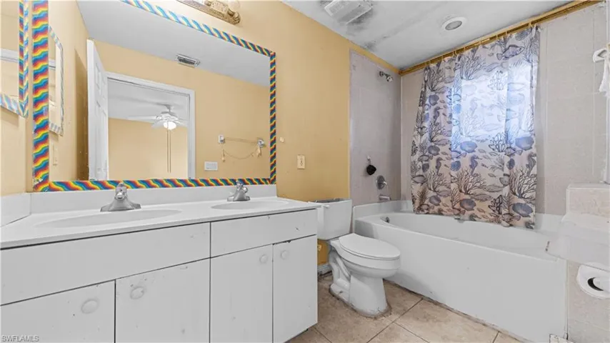 Bathroom with double vanity, light tile patterned floors, shower / bath combo, and a ceiling fan
