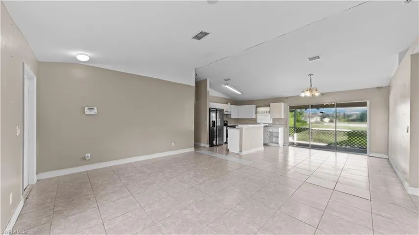 Unfurnished living room featuring a chandelier, lofted ceiling, and light tile patterned flooring