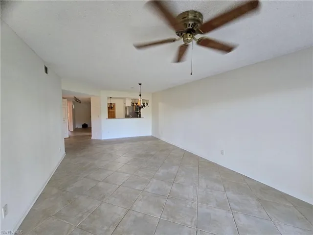 Unfurnished living room with ceiling fan with notable chandelier, a textured ceiling, and light tile patterned flooring