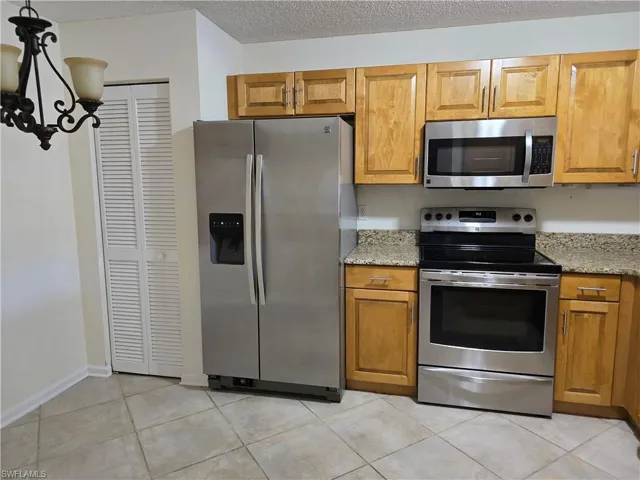 Kitchen featuring appliances with stainless steel finishes, a notable chandelier, granite countertops, a textured ceiling, and light tile patterned flooring