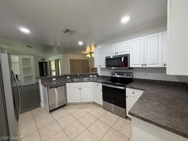 Kitchen featuring white cabinetry, dark speckled countertops, stainless steel appliances, and beige tiled flooring