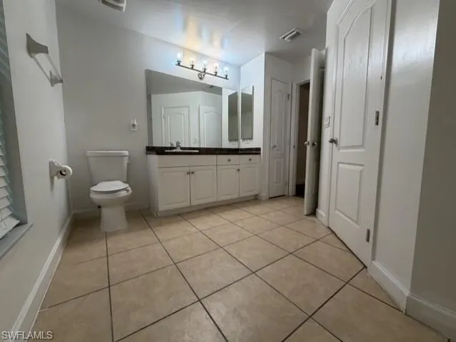 Spacious bathroom featuring large format floor tiles, a white vanity with double cabinet storage, a dark countertop, and an illuminated mirror