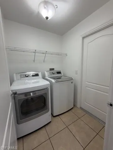Dedicated utility space featuring tile flooring, white walls, and overhead wire shelving