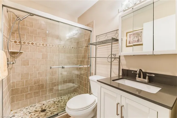 Walk-in shower with natural stone pebble flooring, ceramic tile surround, and glass enclosure