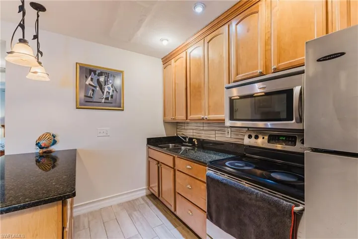 Kitchen featuring wood-finish cabinetry, dark speckled countertops, and stainless steel appliances including a range, microwave, and refrigerator