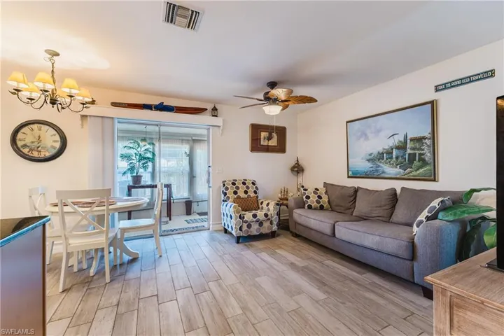 Open-concept living space featuring wood-finish flooring, a ceiling fan with integrated lighting, and a dining area with an overhead chandelier