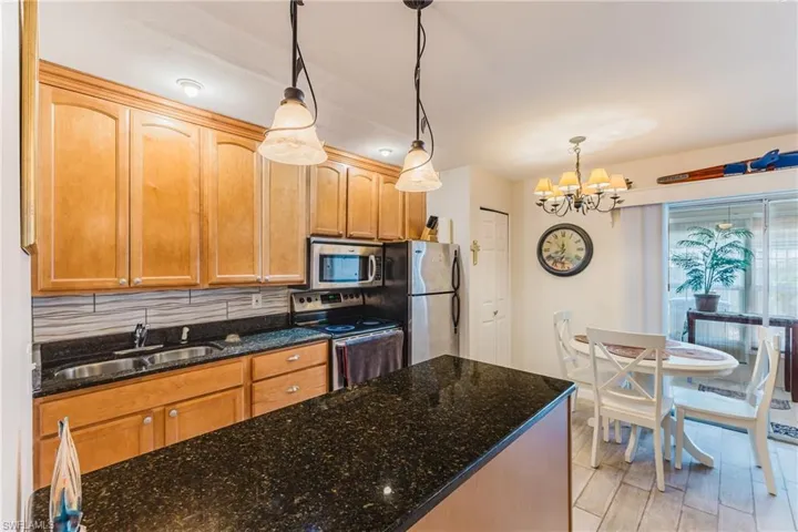 Kitchen featuring wood cabinetry, dark granite-style countertops, stainless steel appliances, and a tiled backsplash