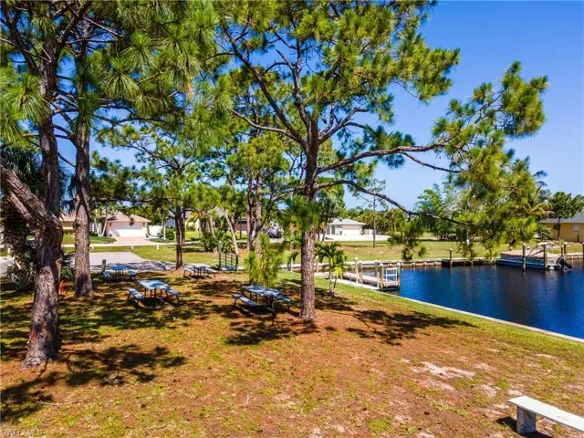 Canal-front property featuring mature pine trees, multiple picnic tables, and a dock with boat slips