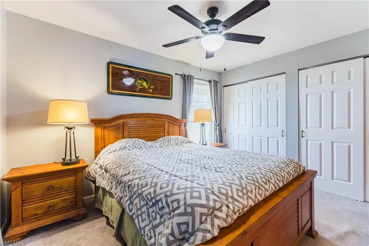 Carpeted room featuring a ceiling fan with integrated lighting, two sets of bi-fold closet doors, and light gray wall paint