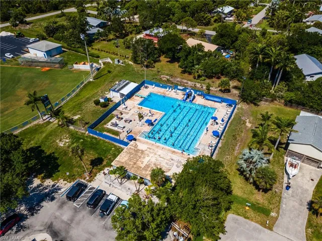 Expansive community swimming pool featuring dedicated lap lanes, multiple lounging areas with sun umbrellas, and adjacent recreational facilities including a baseball field