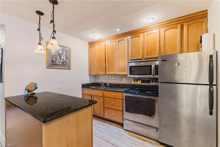 Kitchen featuring light wood cabinetry, dark speckled countertops, and stainless steel appliances