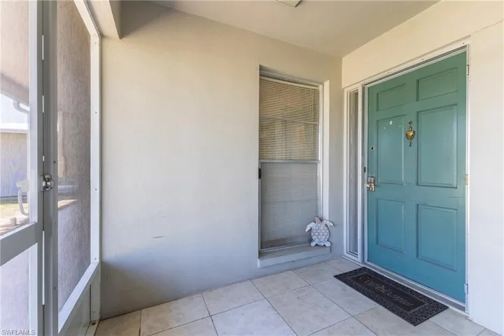 Entryway featuring a paneled turquoise door with brass hardware, sidelite, screened enclosure, and tiled flooring
