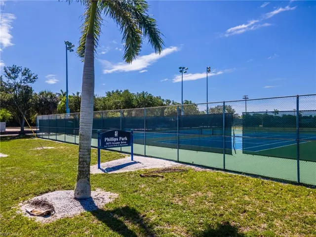 Outdoor tennis courts with chain-link fencing, featuring green and blue playing surfaces, perimeter screening, and overhead lighting fixtures