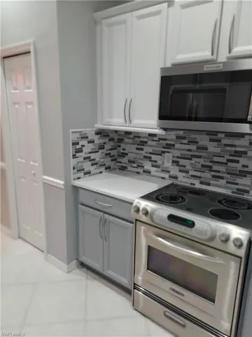 Kitchen featuring tasteful backsplash, light countertops, gray cabinetry, appliances with stainless steel finishes, and white cabinets
