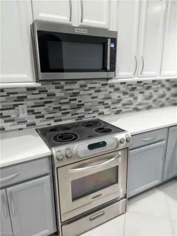 Kitchen with stainless steel appliances, light countertops, white cabinetry, and tasteful backsplash
