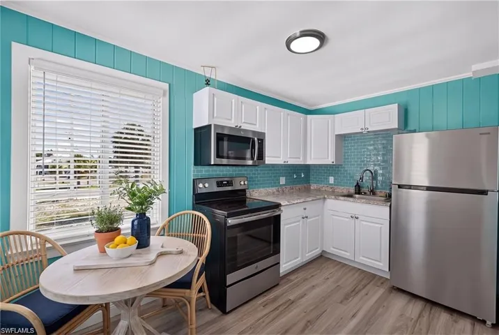2101 Cottage North Unit - Kitchen featuring white cabinetry, stainless steel appliances, a tile backsplash, wood-finish flooring, and a large window- VIRTUALLY STAGED