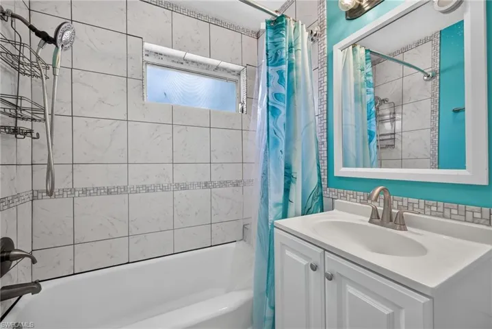 2401 Cottage Ave Unit 1 Bathroom featuring a built-in bathtub with a curved shower rod, tile surround with decorative accent, and a horizontal frosted window