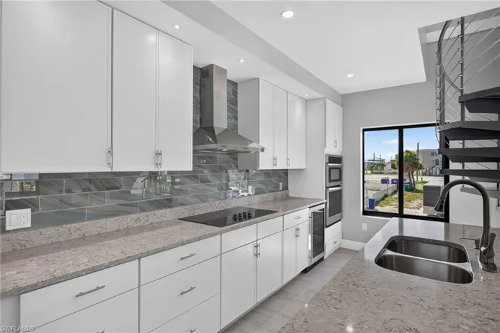 71 Mango Unit 1  Modern kitchen featuring white cabinetry, integrated stainless steel appliances, a tile backsplash, and stone countertops