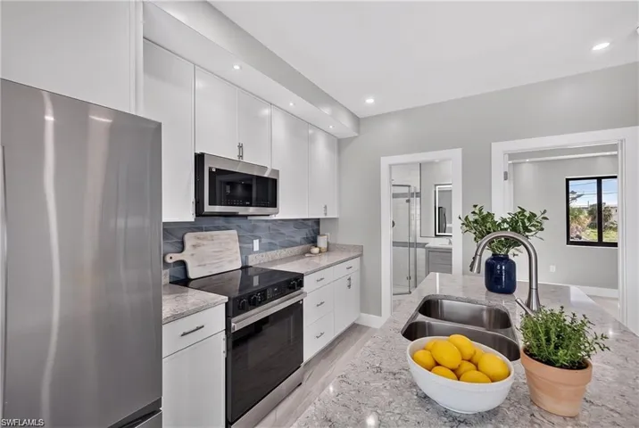 71 Mango North Unit - Kitchen featuring white cabinetry, stainless steel appliances, a stone countertop, a tile backsplash, and an integrated sink with a gooseneck faucet - VIRTUALLY STAGED