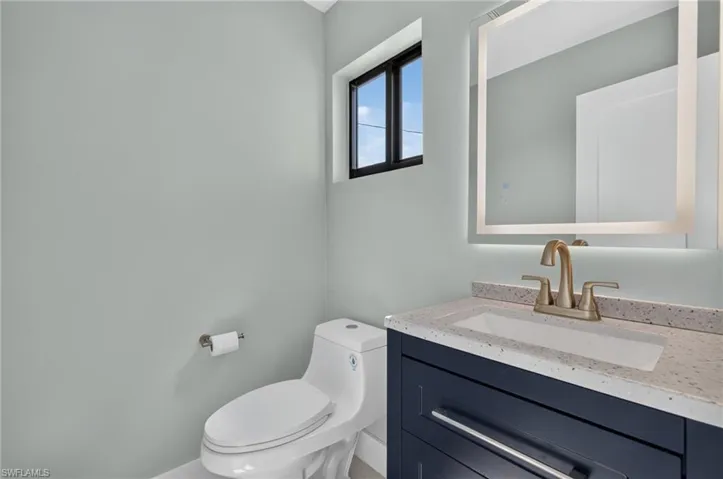 71 Mango Unit 1 Modern half-bathroom featuring a dark blue vanity with a light speckled countertop, an integrated rectangular sink, and a gold-toned faucet