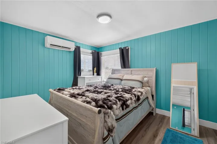 2101 Cottage North Unit - Wood-finish flooring, accent wall with vertical paneling, windows with horizontal blinds, ceiling-mounted light fixture, and ductless mini-split system