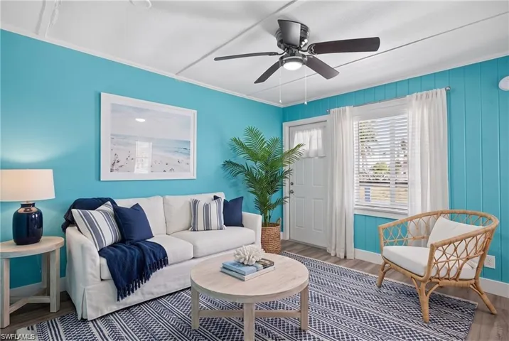 2101 Cottage North Unit - Wood-finish flooring with vibrant wall paneling, a ceiling fan with integrated lighting, and a white entry door with a window- VIRTUALLY STAGED