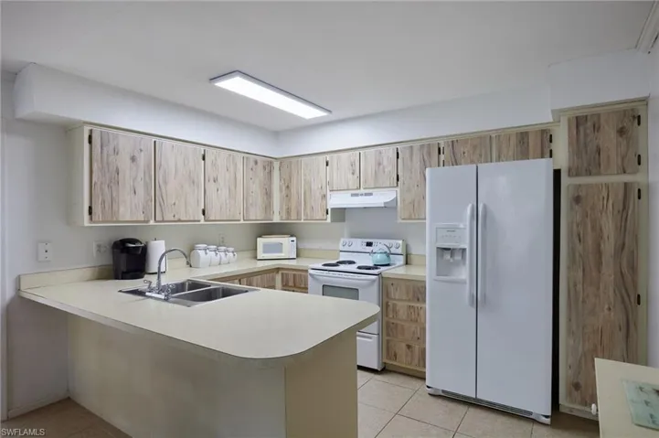Kitchen with white appliances, light countertops, a peninsula, light tile patterned floors, and under cabinet range hood
