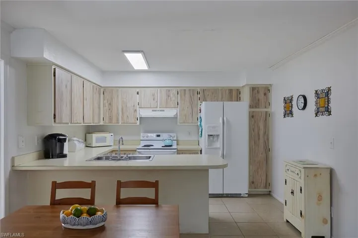 Kitchen with white appliances, light countertops, under cabinet range hood, light tile patterned floors, and a peninsula
