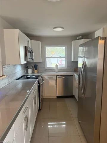 Kitchen featuring tasteful backsplash, dishwasher, refrigerator, stove, and white cabinetry