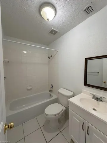 Full bathroom with light tile patterned floors, vanity, bathing tub / shower combination, a textured ceiling, and a textured wall