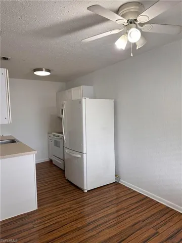 Kitchen featuring white cabinetry, white appliances, light countertops, dark wood-type flooring, and ceiling fan
