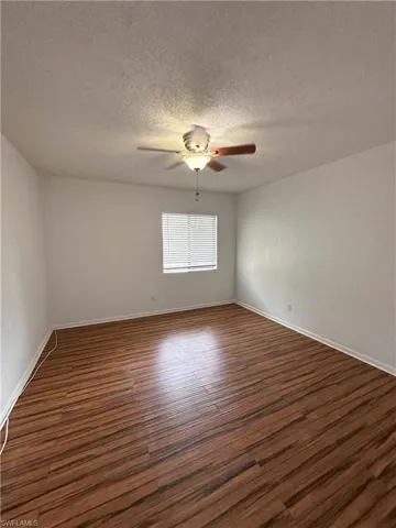 Empty room featuring dark wood-style flooring, a textured ceiling, and a ceiling fan