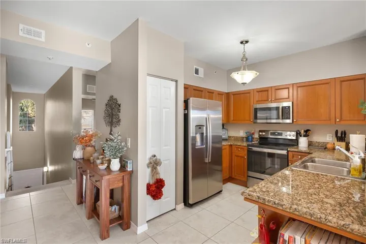 Kitchen featuring appliances with stainless steel finishes, light stone counters, brown cabinetry, light tile patterned floors, and decorative light fixtures