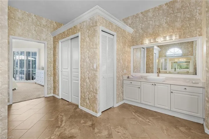 Bathroom with a closet, vanity, baseboards, and wallpapered walls