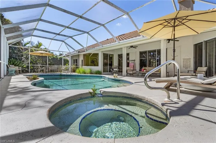 View of pool featuring glass enclosure, a patio, a pool with connected hot tub, and a ceiling fan