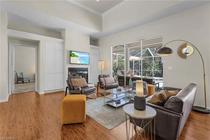 Living area with a sunroom, light wood-style flooring, crown molding, and a glass covered fireplace