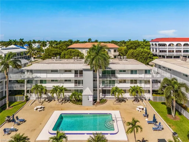 Multi-level building with individual balconies, central swimming pool, and surrounding hardscaped patio